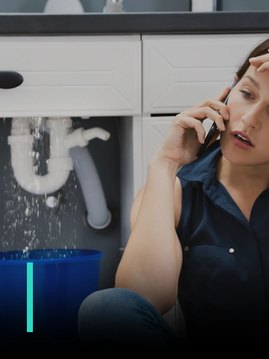 Una mujer llama por teléfono frente a una cañería que gotea